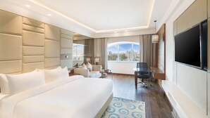 A modern hotel room with a large bed, a desk, a chair, a TV, and a view of the city. - Radisson Jaipur City Center (Jaipur)