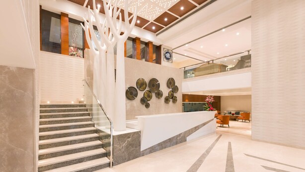 A modern hotel lobby with a marble staircase, a reception desk, and a decorative wall with circular mirrors. - Radisson Jaipur City Center (Jaipur)