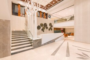 Un moderno vestíbulo de hotel con una escalera de mármol, un mostrador de recepción y una pared decorativa con espejos circulares.