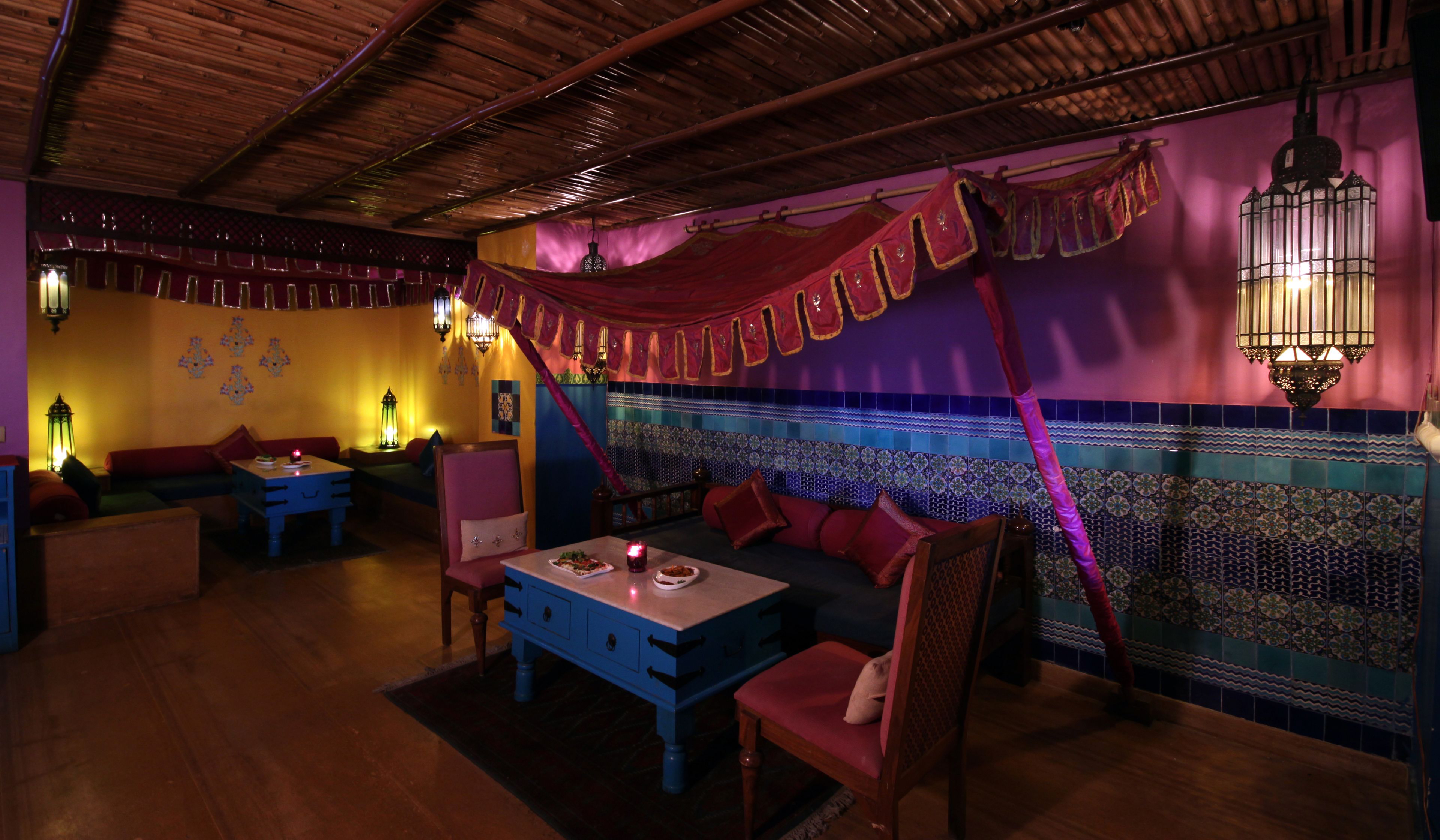 A cozy interior with a wooden ceiling, a sofa set, a dining table, and patterned wall tiles.