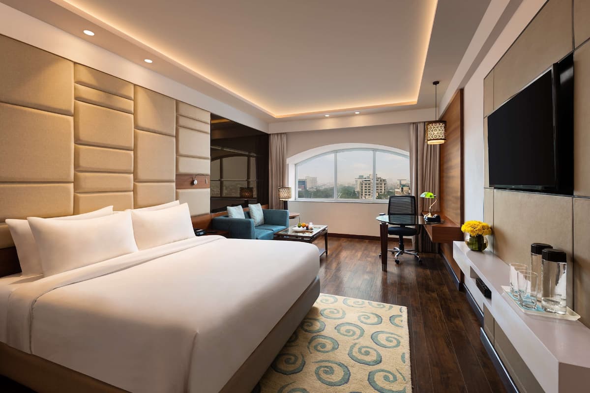 A modern hotel room with a large bed, a desk, a sofa, and a TV.
