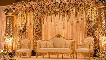 A stage with a sofa and two chairs, surrounded by floral arrangements and draped curtains.
