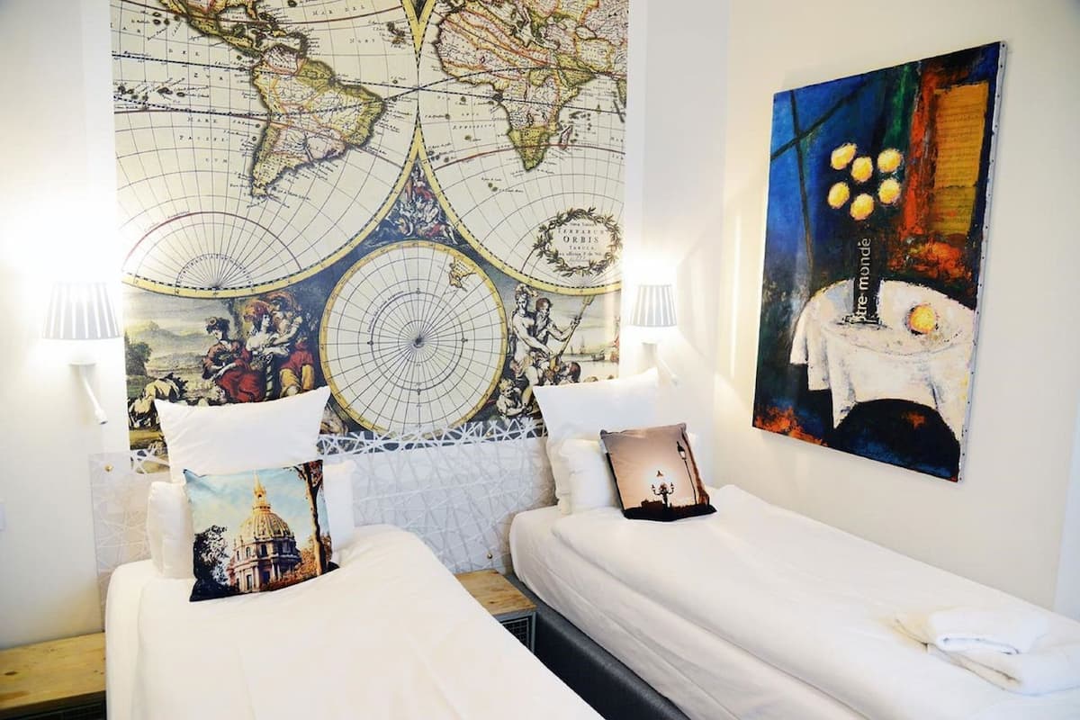 Habitación de hotel con dos camas, un gran mapa mundial en la pared y una pintura de una mesa iluminada con velas.