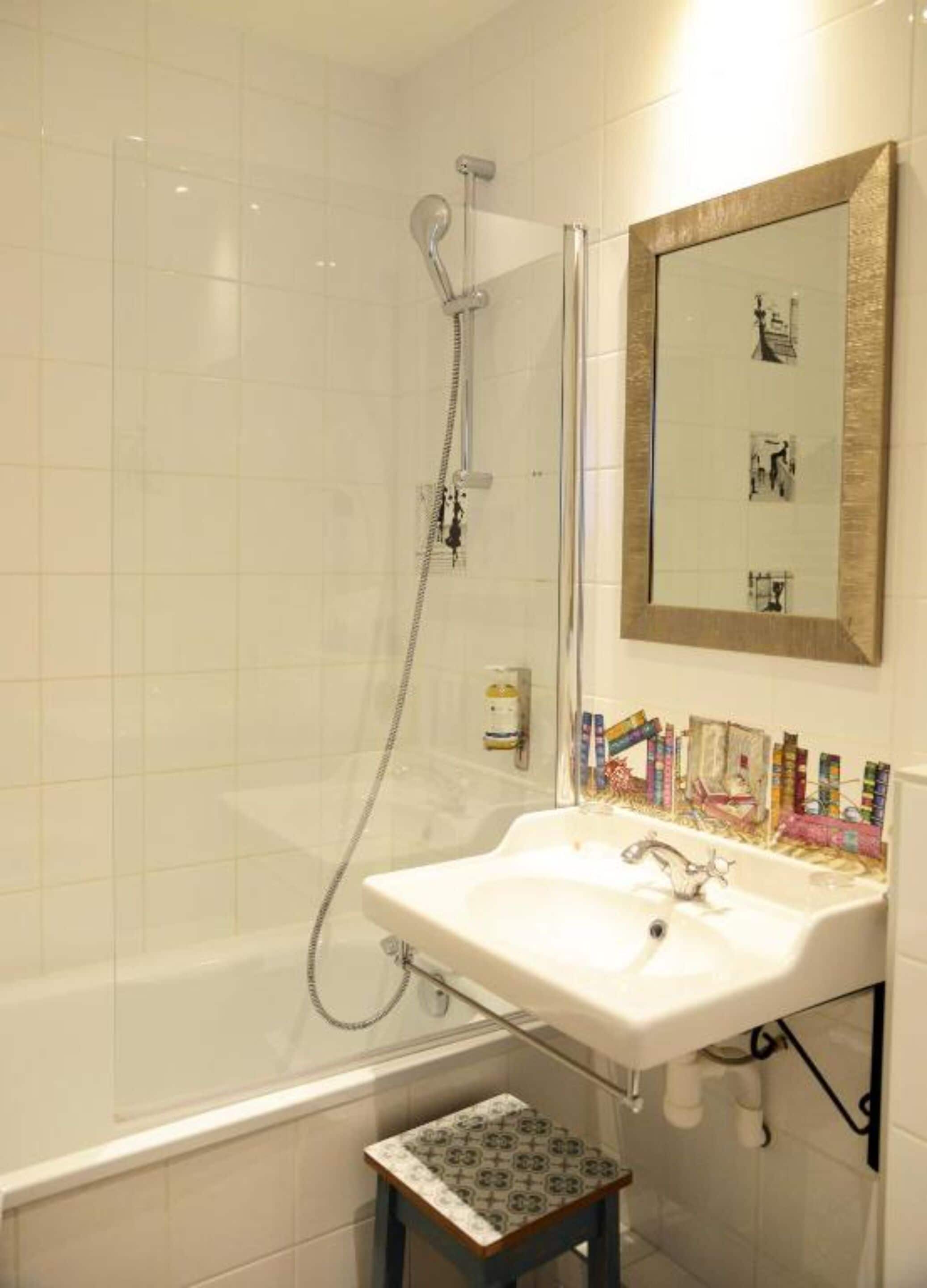 A bathroom with a glass-enclosed shower, a white sink, and a small step stool.