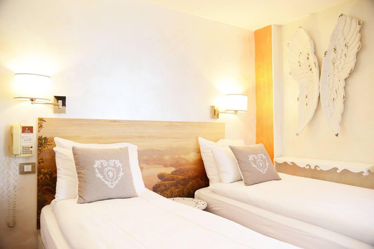 Habitación de hotel con dos camas, cabecera de madera, lámparas fijadas a la pared y un adorno mural.