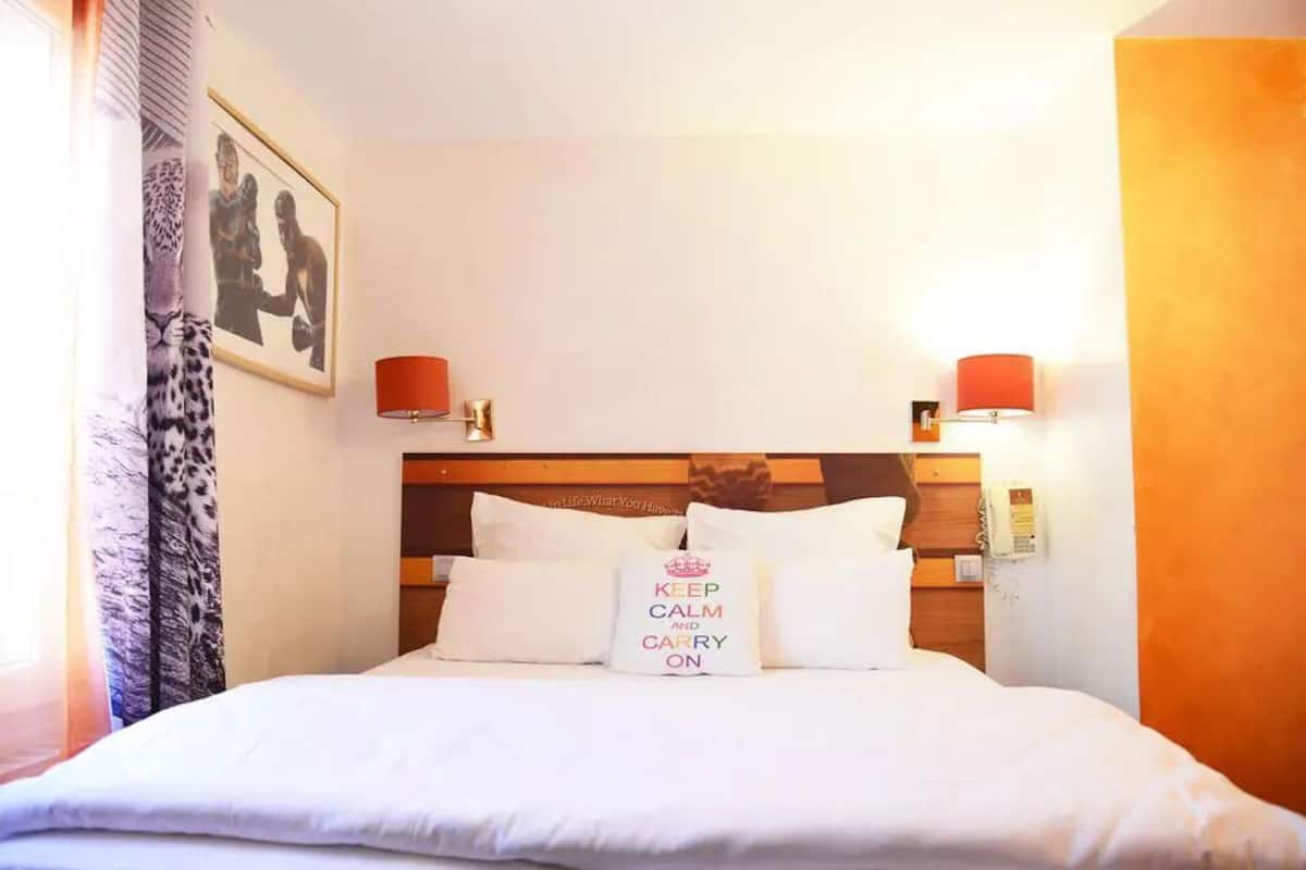 Una habitación de hotel con una cama bien hecha, un cuadro en la pared y una lámpara de noche.