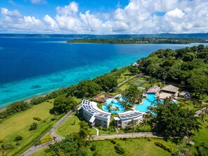 Vista aérea de un resort con una gran piscina, abundante vegetación y vistas al océano.