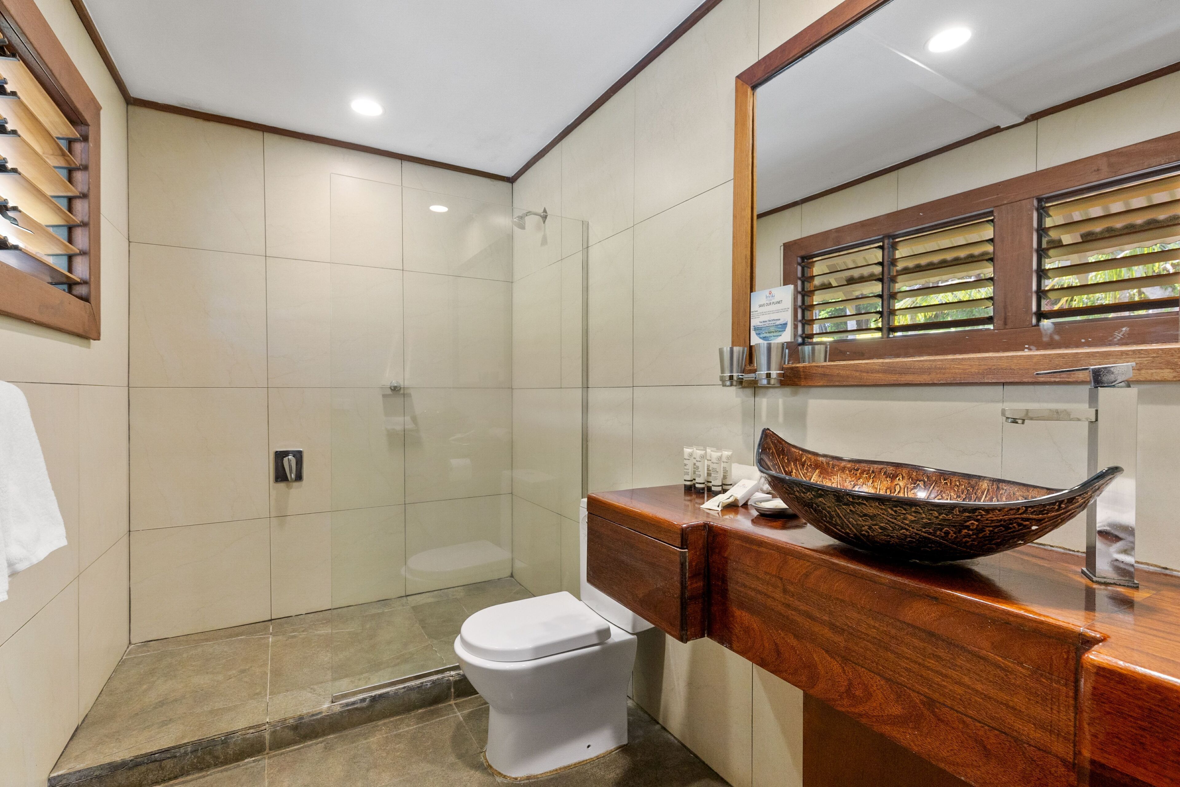 A modern bathroom with a white toilet, a glass-enclosed shower, and a wooden vanity with a large bowl sink.