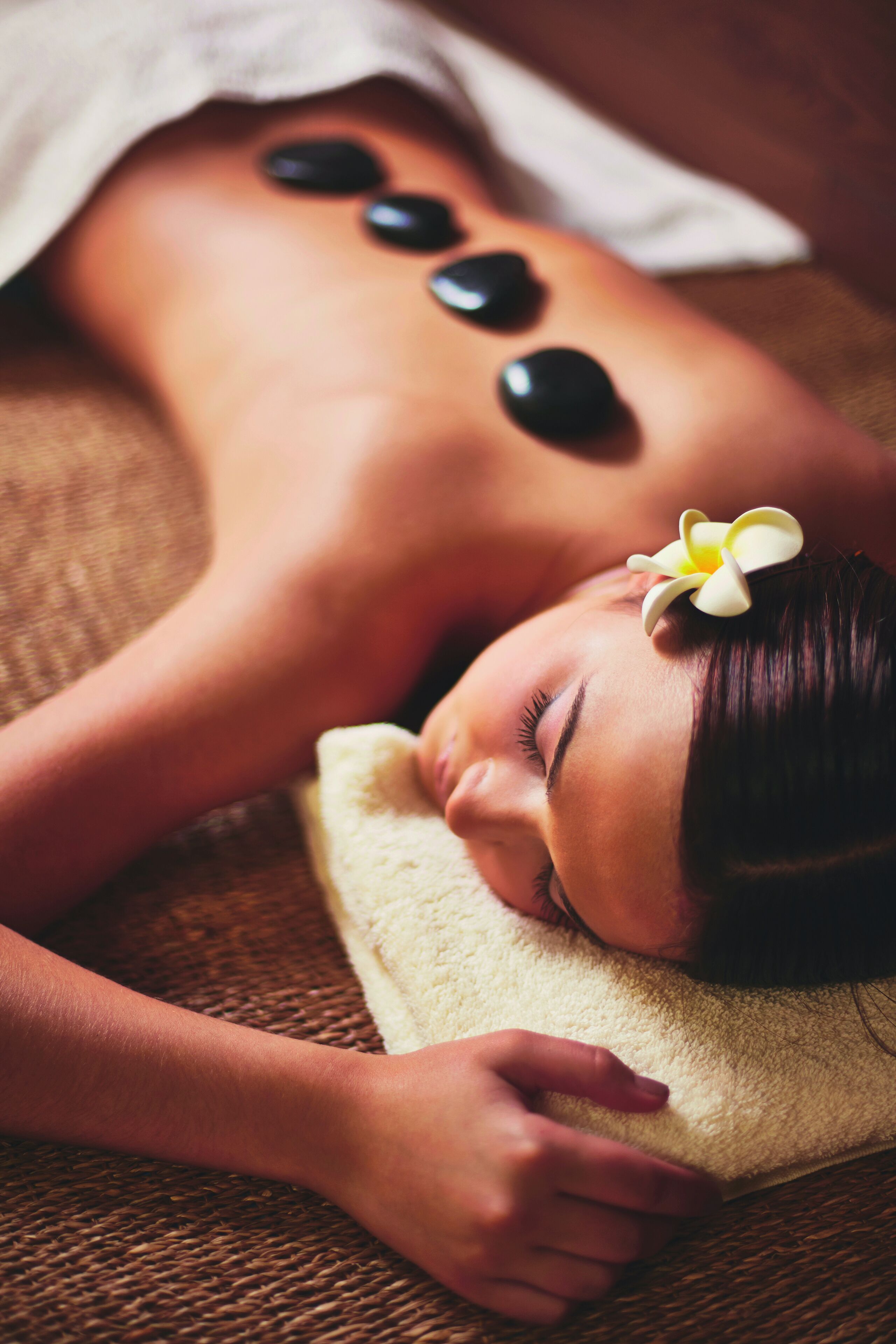 A person receiving a massage with stones on their back, lying on a towel.