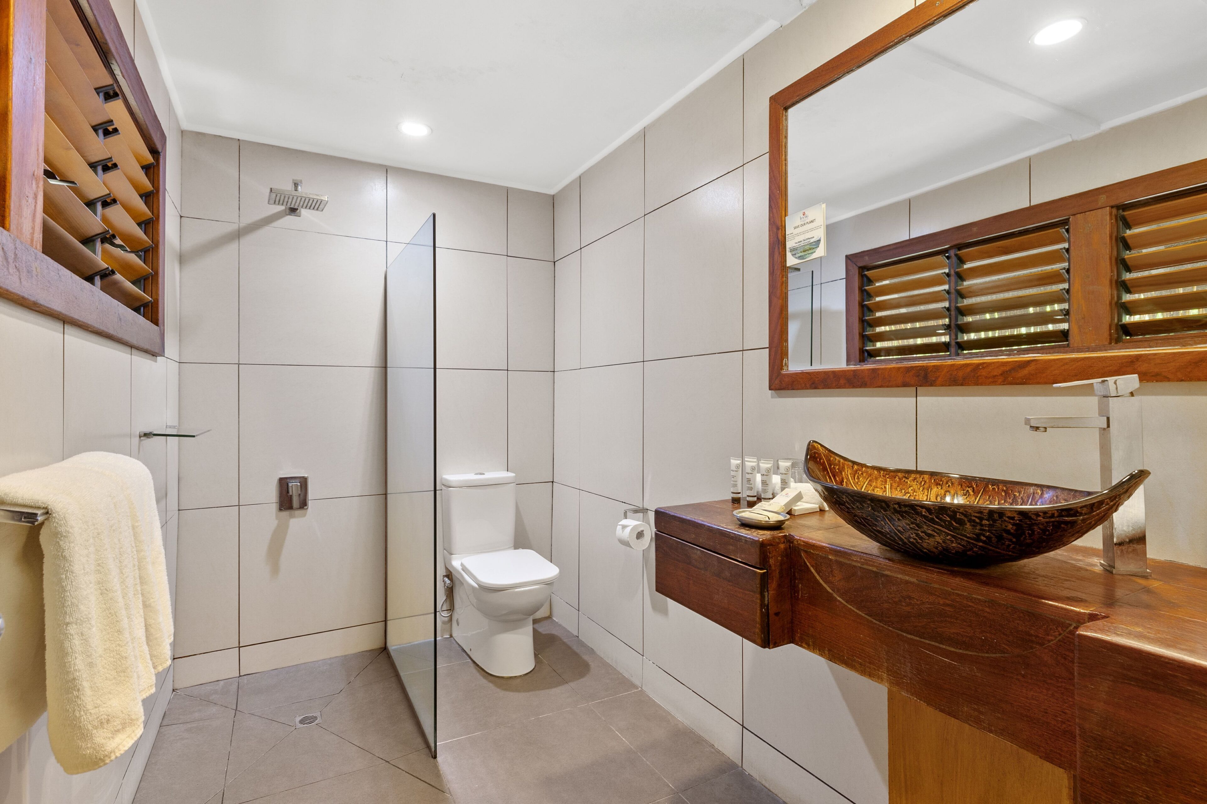 A modern bathroom with a glass shower enclosure, a white toilet, and a wooden vanity with a large vessel sink.