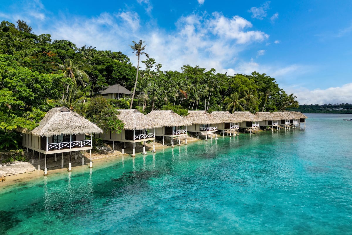 Wasserbungalows mit Strohdächern und weißen Geländern, verbunden durch Wege über klares, türkisfarbenes Wasser.