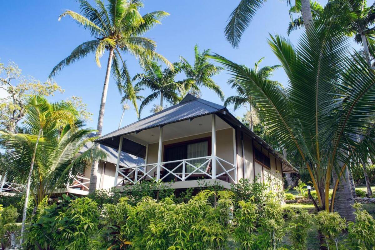 Ein Bungalow mit Balkon, umgeben von üppiger Vegetation und Palmen.