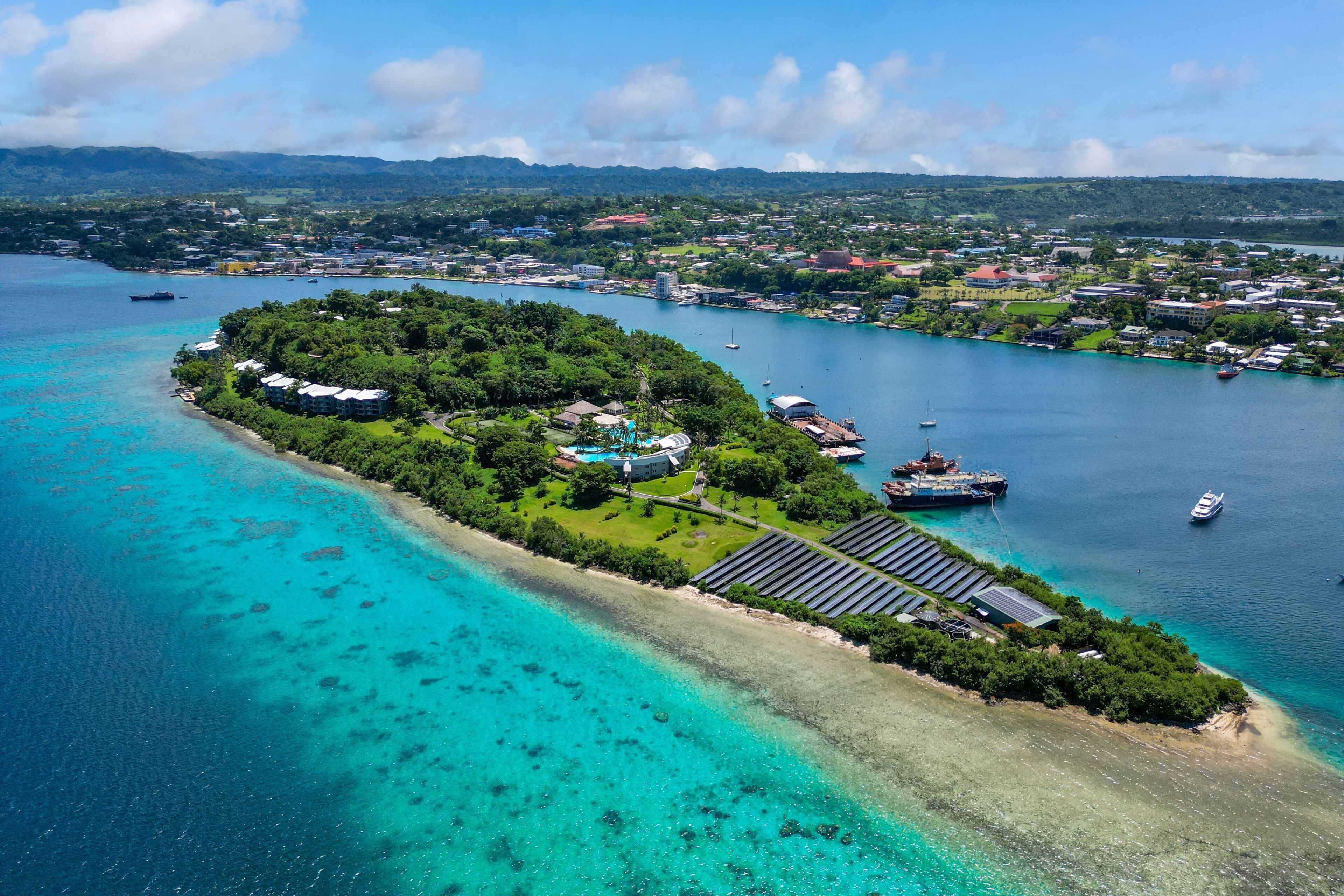 Vista aérea de una isla tropical con un puerto deportivo, abundante vegetación y aguas turquesas cristalinas.