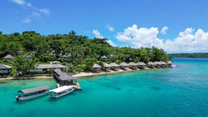 Un resort con bungalows sobre el agua, con techos de paja, un muelle para barcos y aguas turquesas cristalinas.
