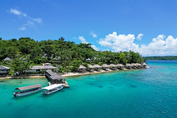 Un resort con bungalows sobre el agua, con techos de paja, un muelle para barcos y aguas turquesas cristalinas.