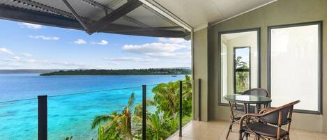 A balcony with a view of the ocean and a table with chairs.