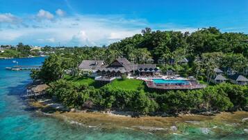 An aerial view of a tropical resort with a large pool, multiple guest villas, and lush greenery.