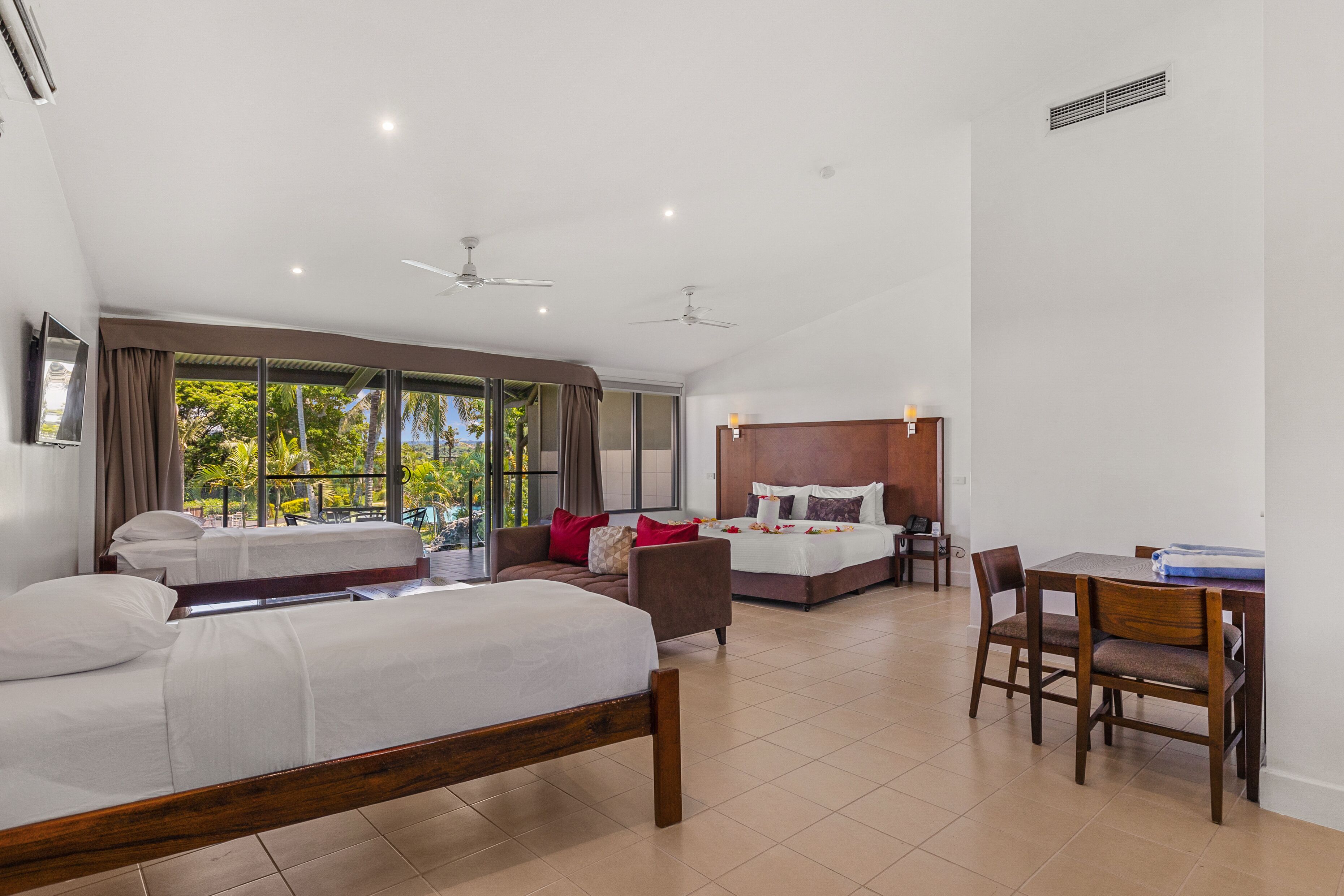 A hotel room with two beds, a dining table, and a view of the outdoors.