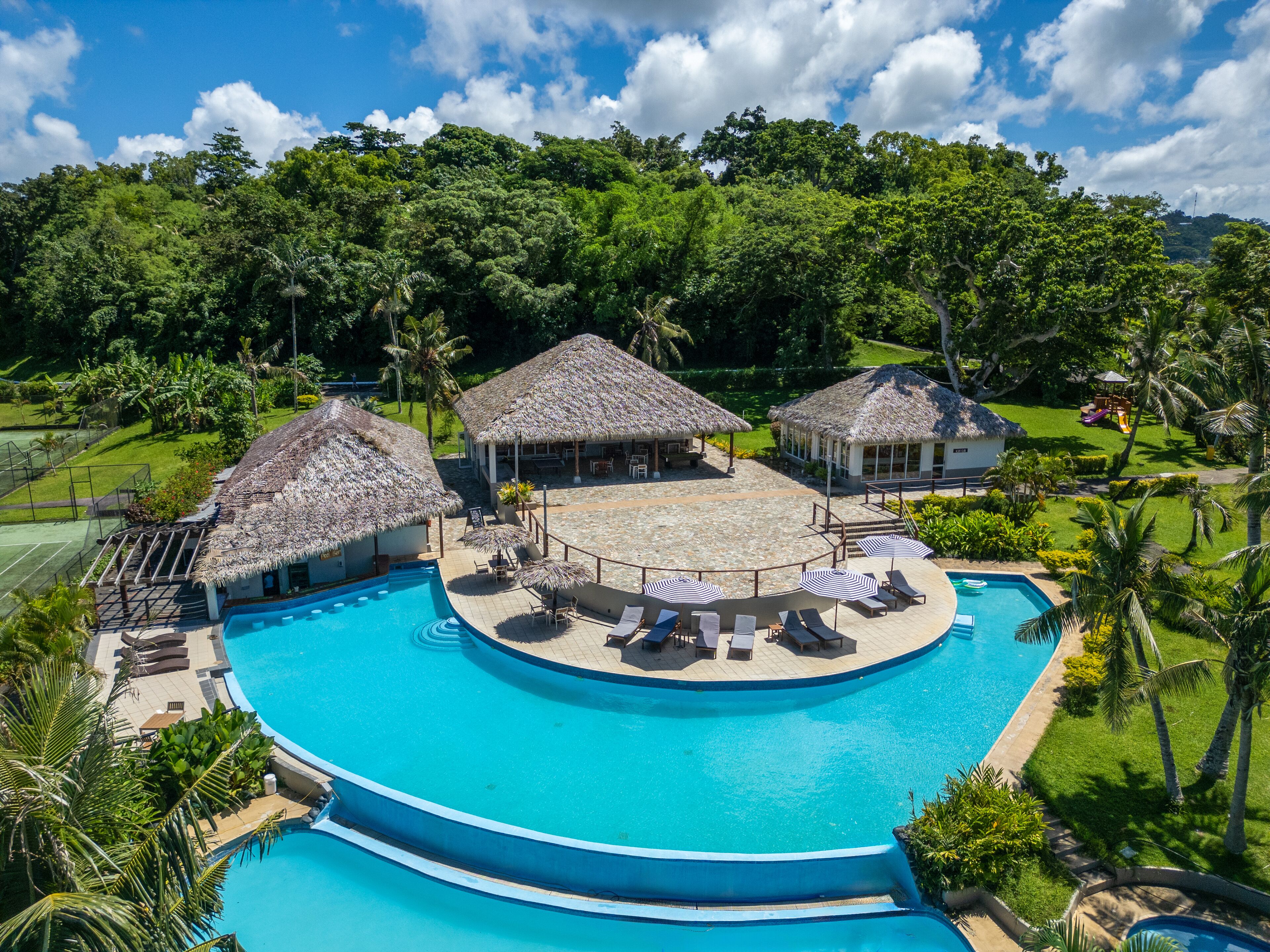 A resort with a large swimming pool, thatched-roof structures, and lush greenery.
