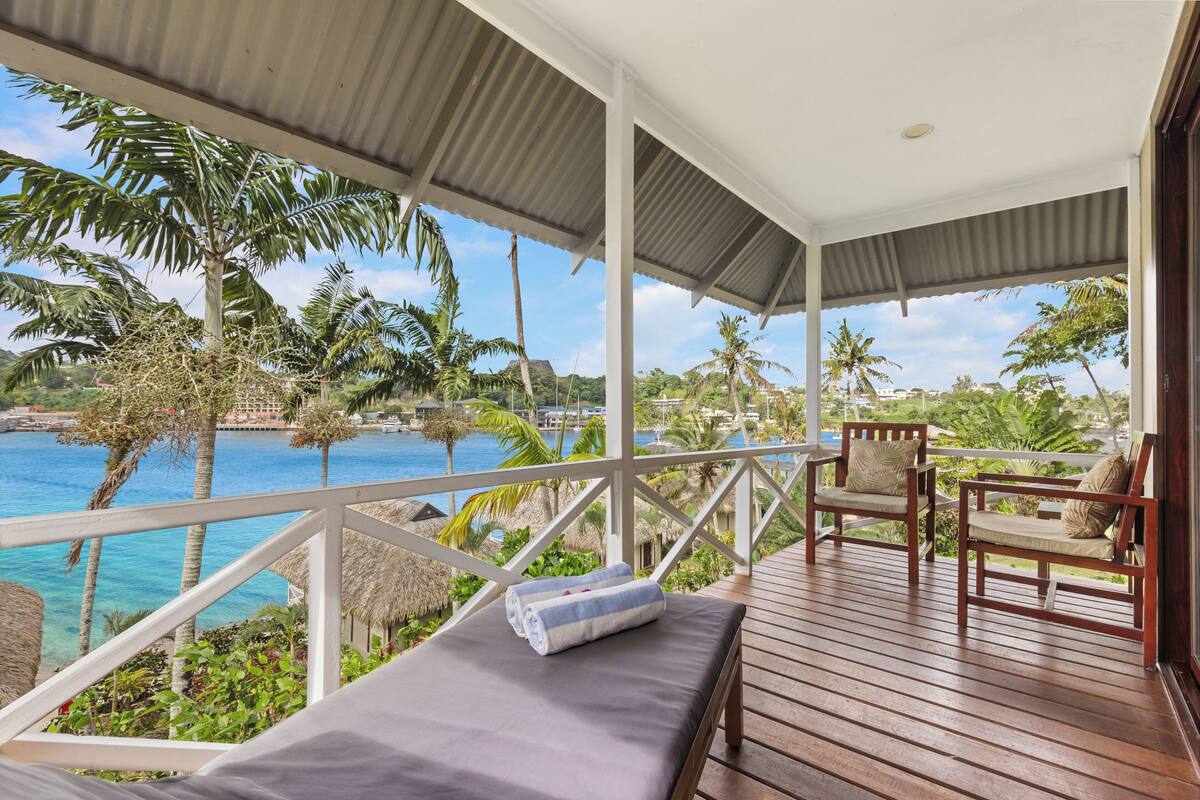 Eine Holzterrasse mit Lounge-Bereich mit Blick auf einen tropischen Strand und das Meer.
