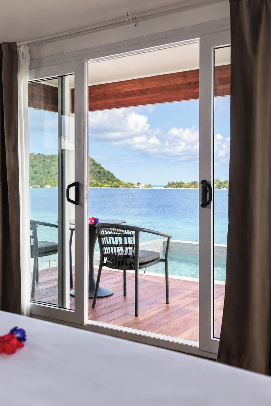 A room with a large sliding glass door leading to a deck with a view of a body of water and a distant island.