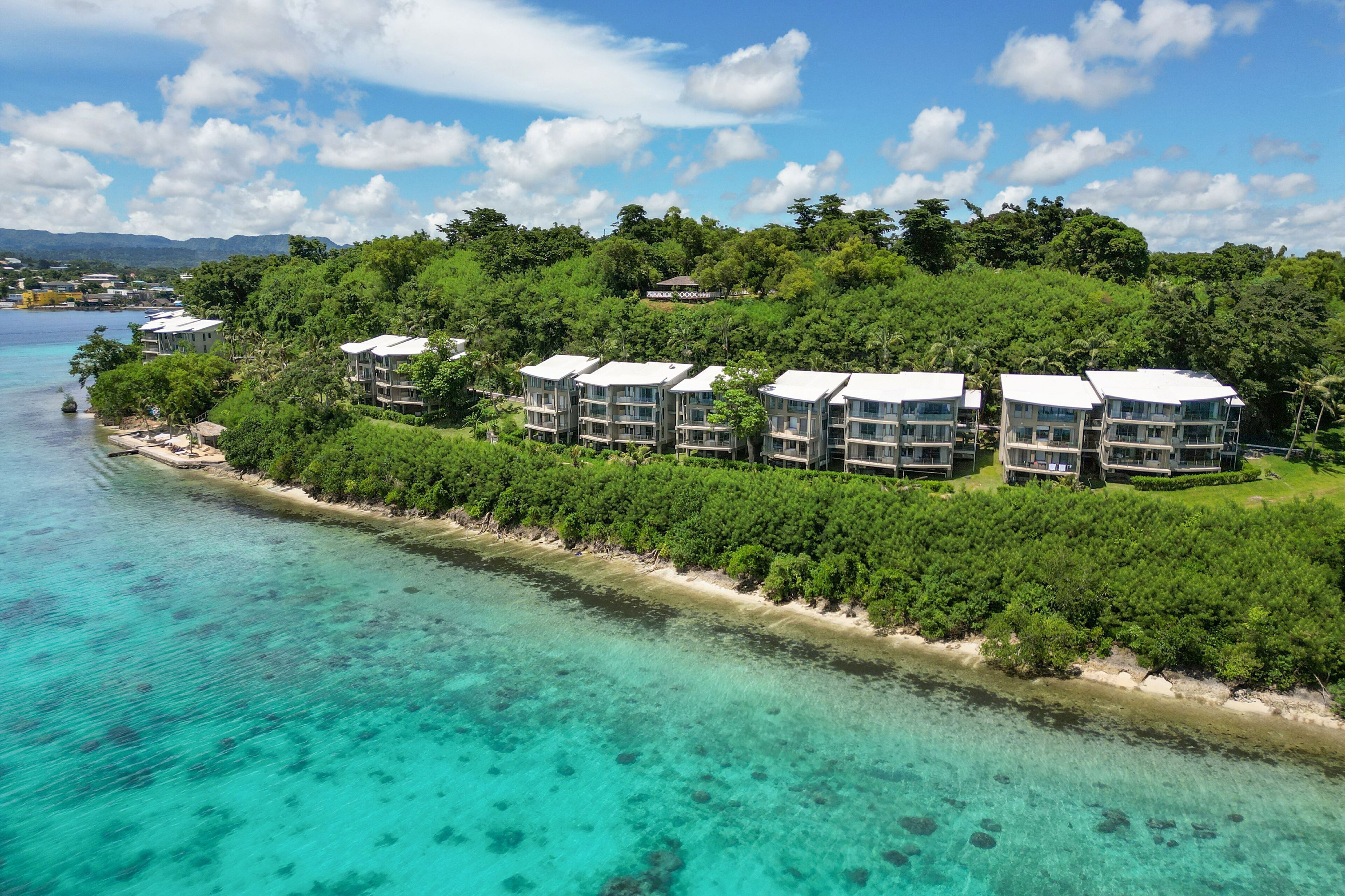 A resort with multiple buildings, a beachfront, and clear turquoise waters.