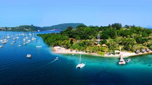 Una isla con una playa, rodeada de aguas azules cristalinas y numerosos barcos.