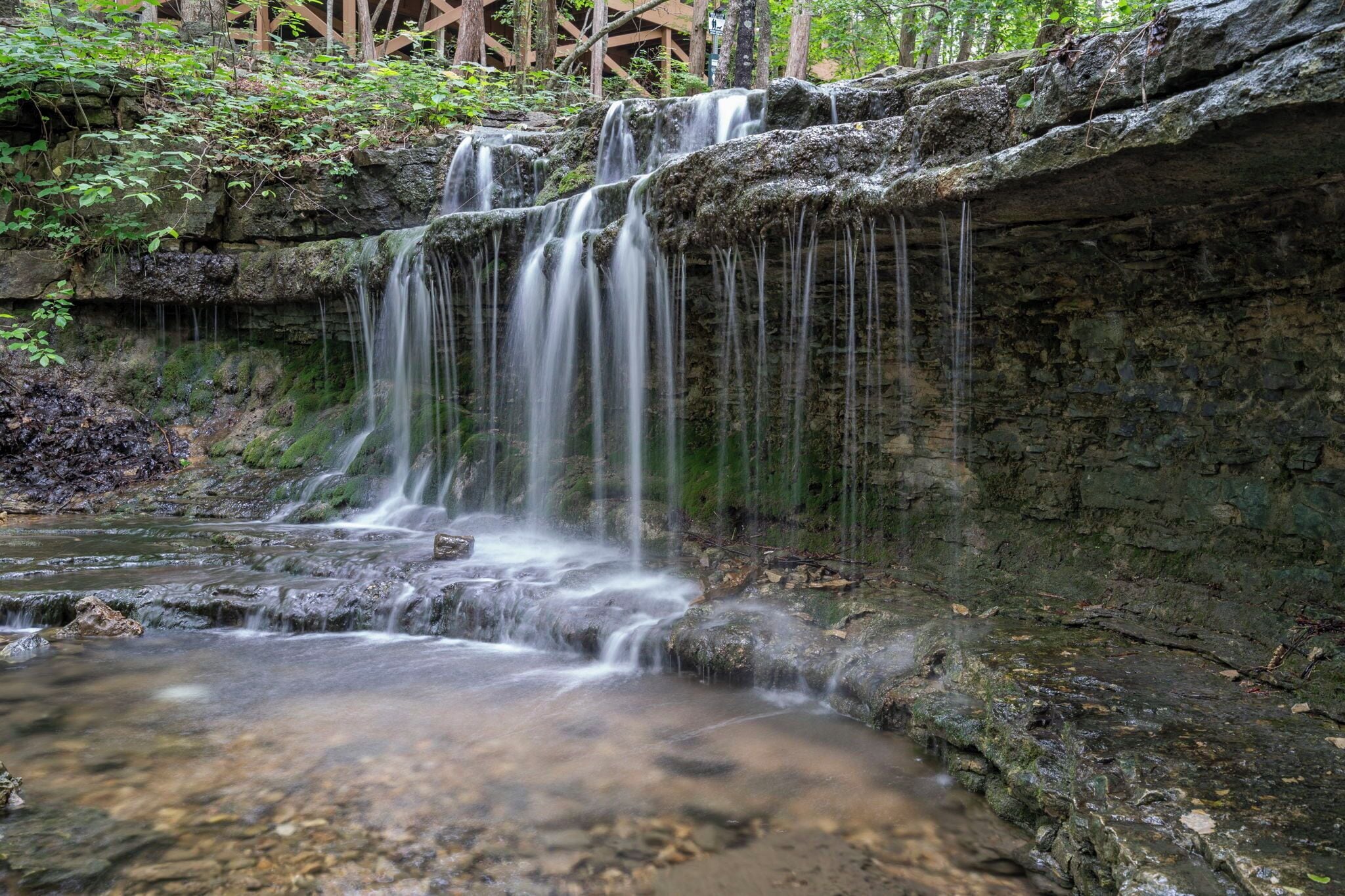 Une cascade d’eau se déversant sur des rochers couverts de mousse, dans une étendue d’eau claire.
