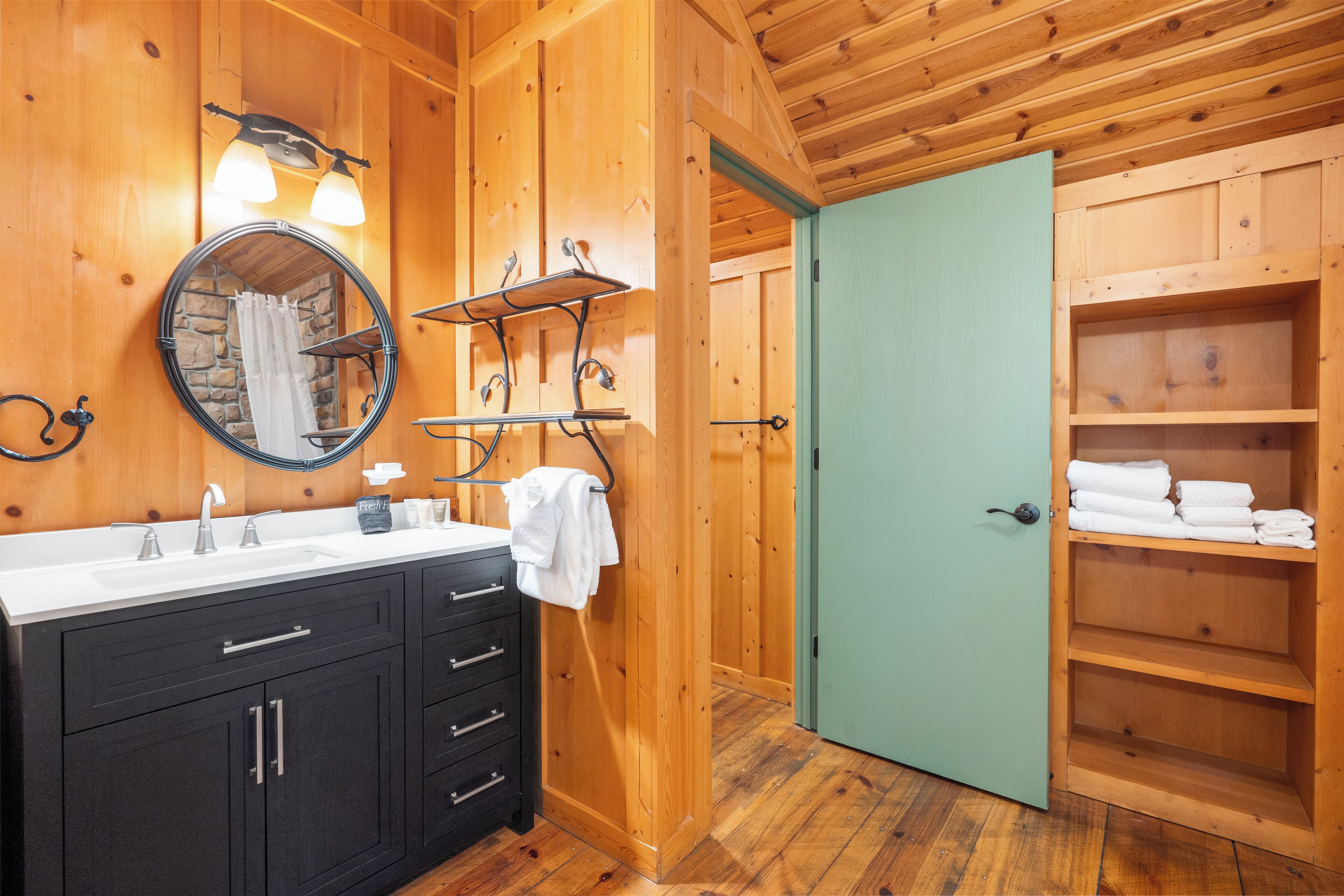 A wooden bathroom with a sink, mirror, towel rack, and shelves.