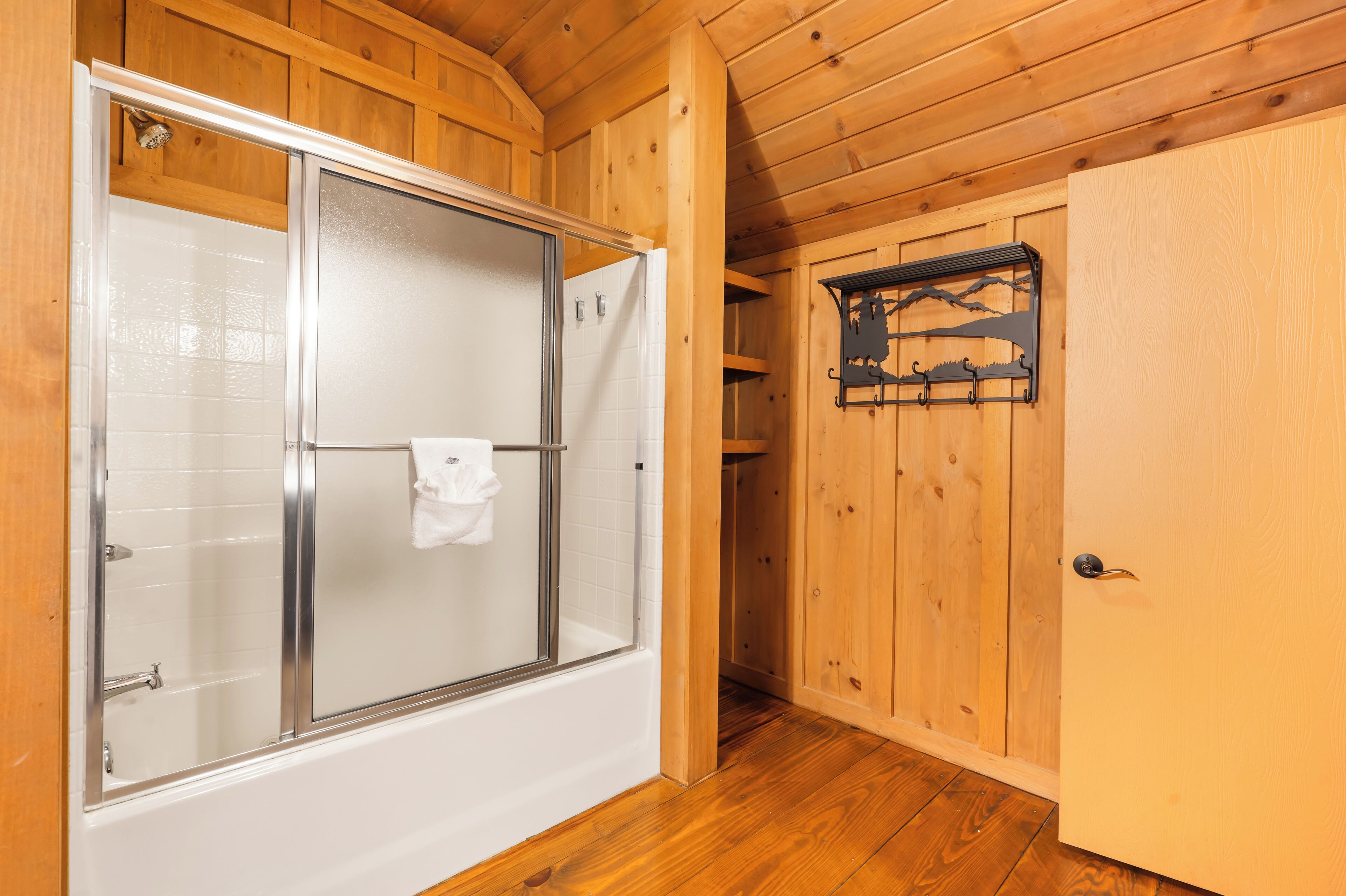 Ein Holzinnenraum mit einer gläsernen Dusche, einer weißen Tür und einem Holzboden.