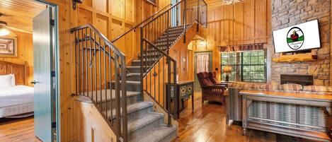 A wooden interior with a staircase, a fireplace, and a stone wall.