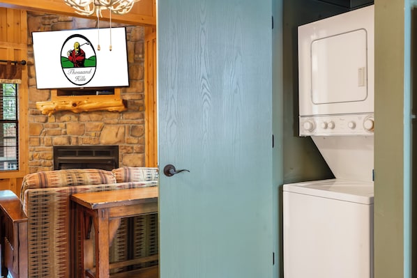 A room with a stone wall, a mounted television, a wooden bench, and a white appliance. - Cabins at Green Mountain (Branson)