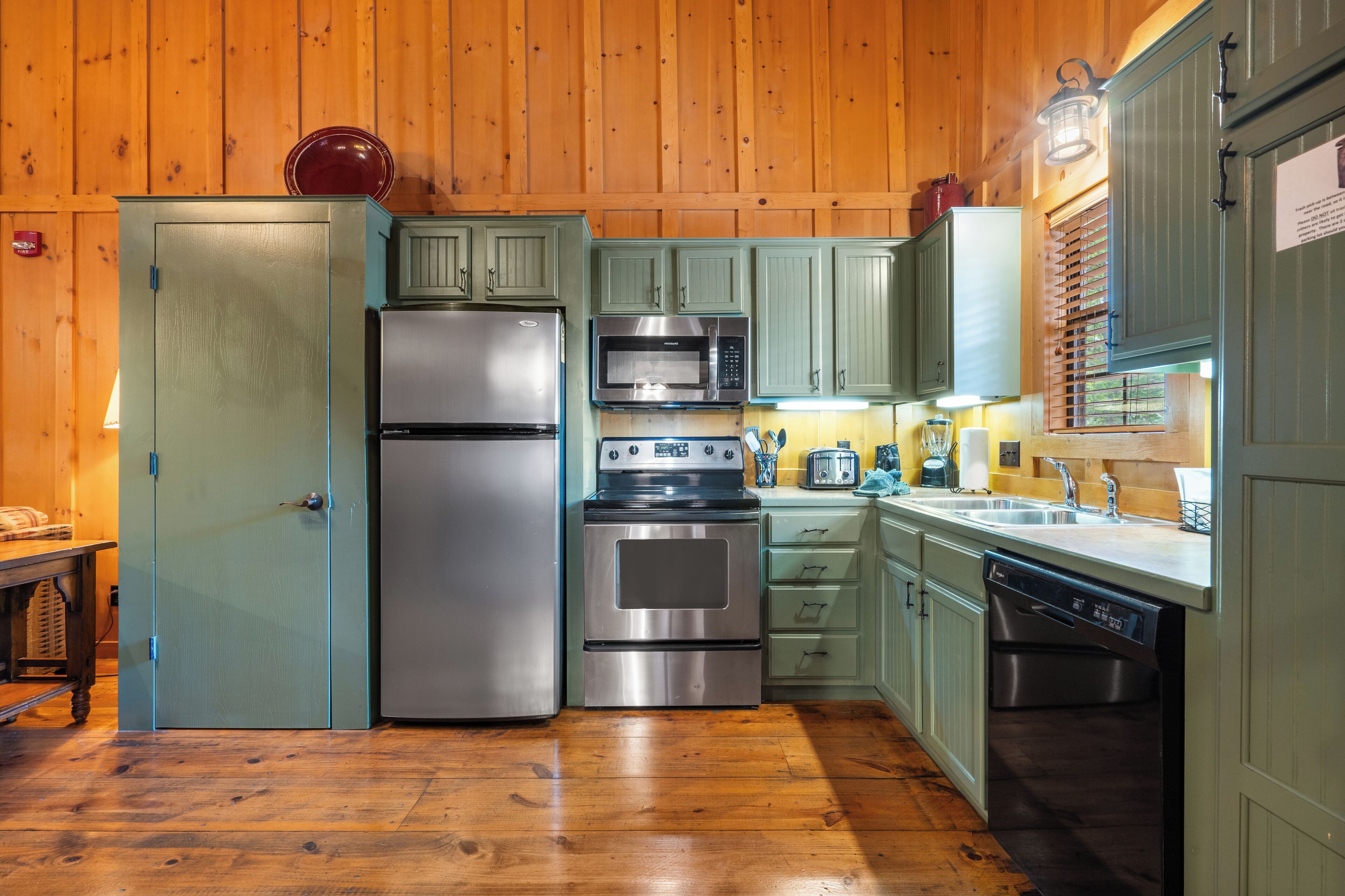 A compact kitchen with wooden cabinets, stainless steel appliances, and a wooden floor.