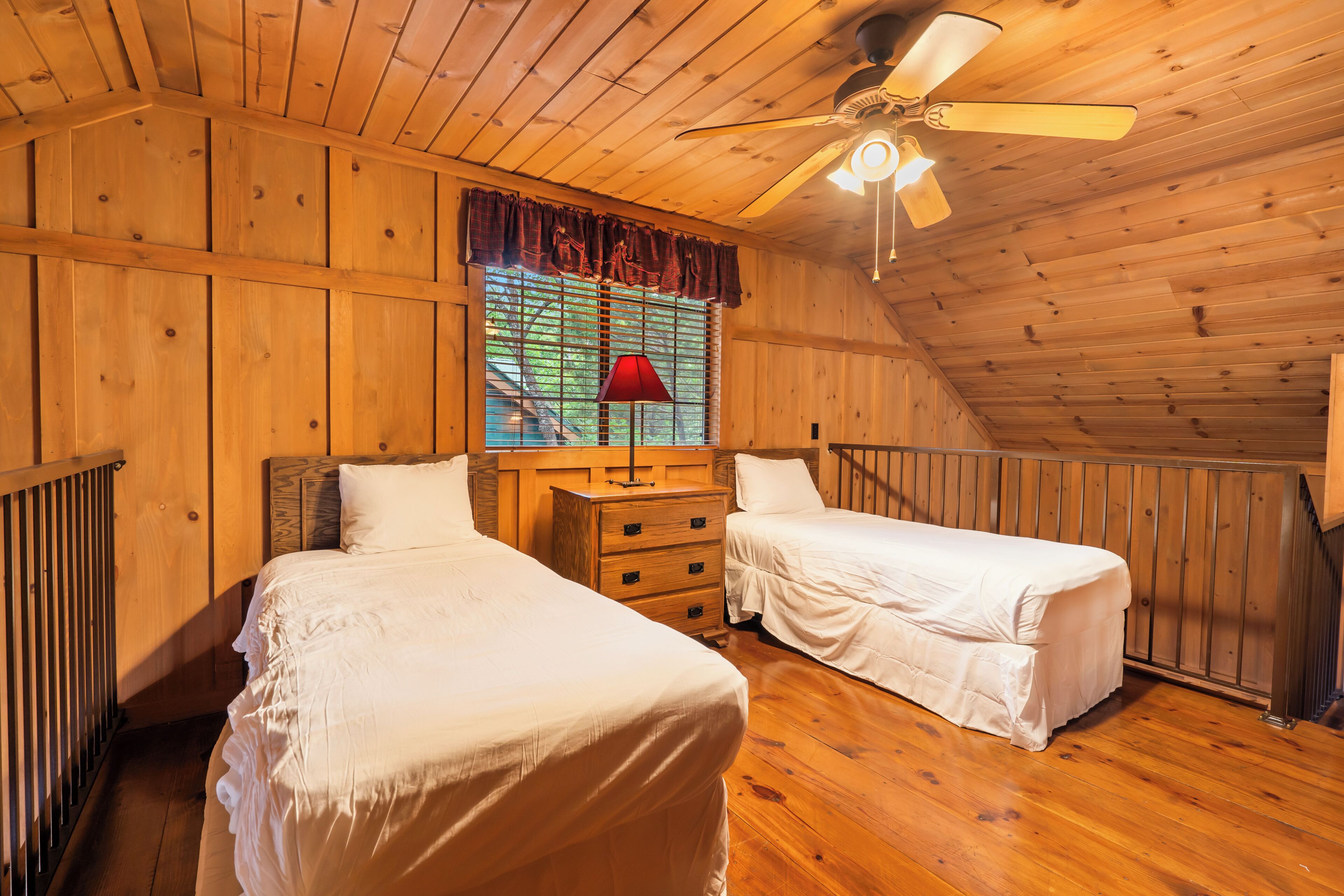 Una habitación de madera con dos camas, un aparador y una ventana con persianas.