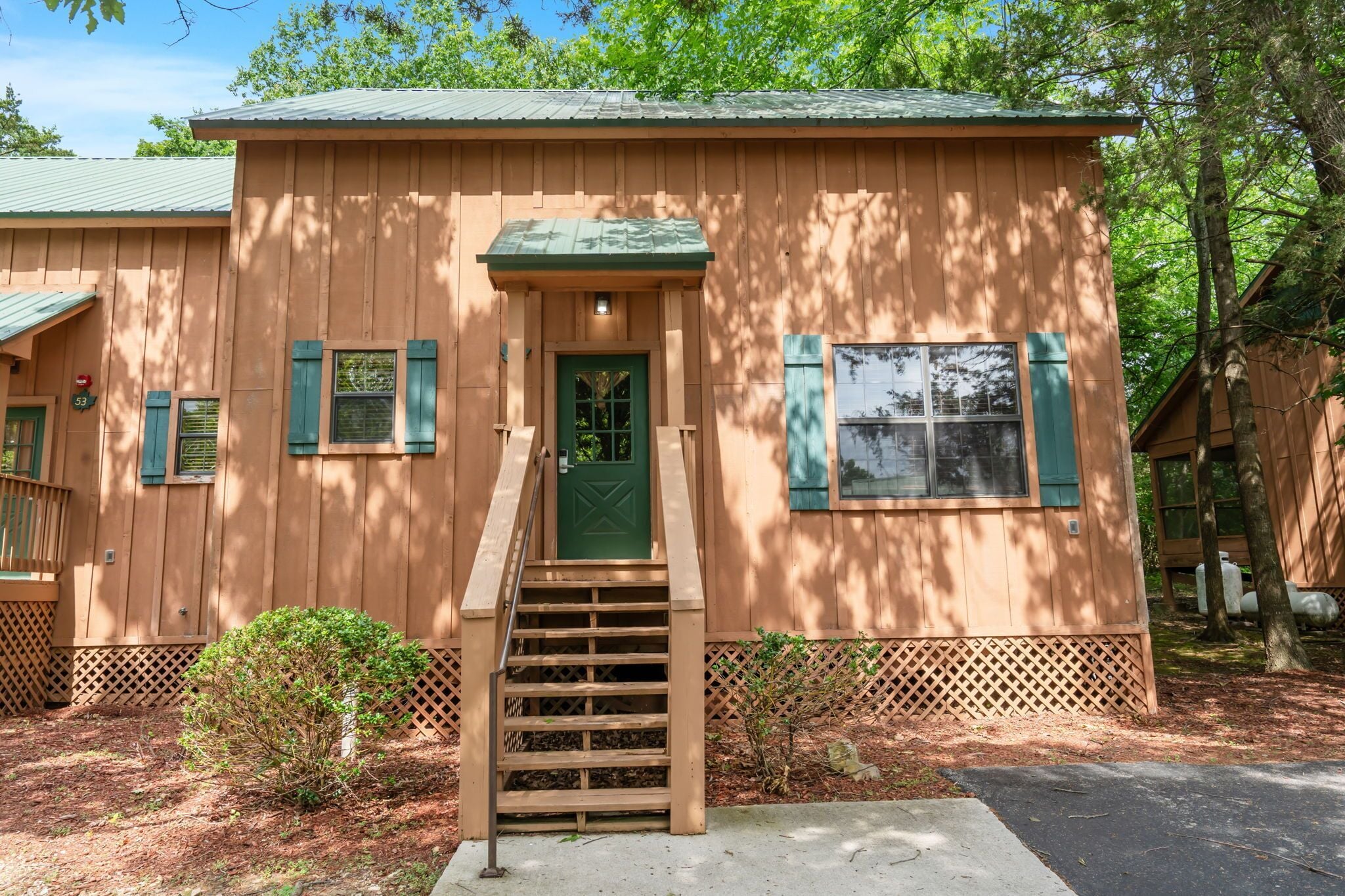 A wooden cabin with a green door, a small porch, and a staircase leading to the entrance.