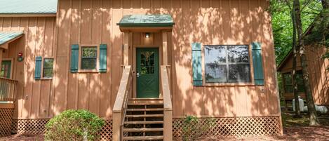 A wooden cabin with a green door, a small porch, and a staircase leading to the entrance.