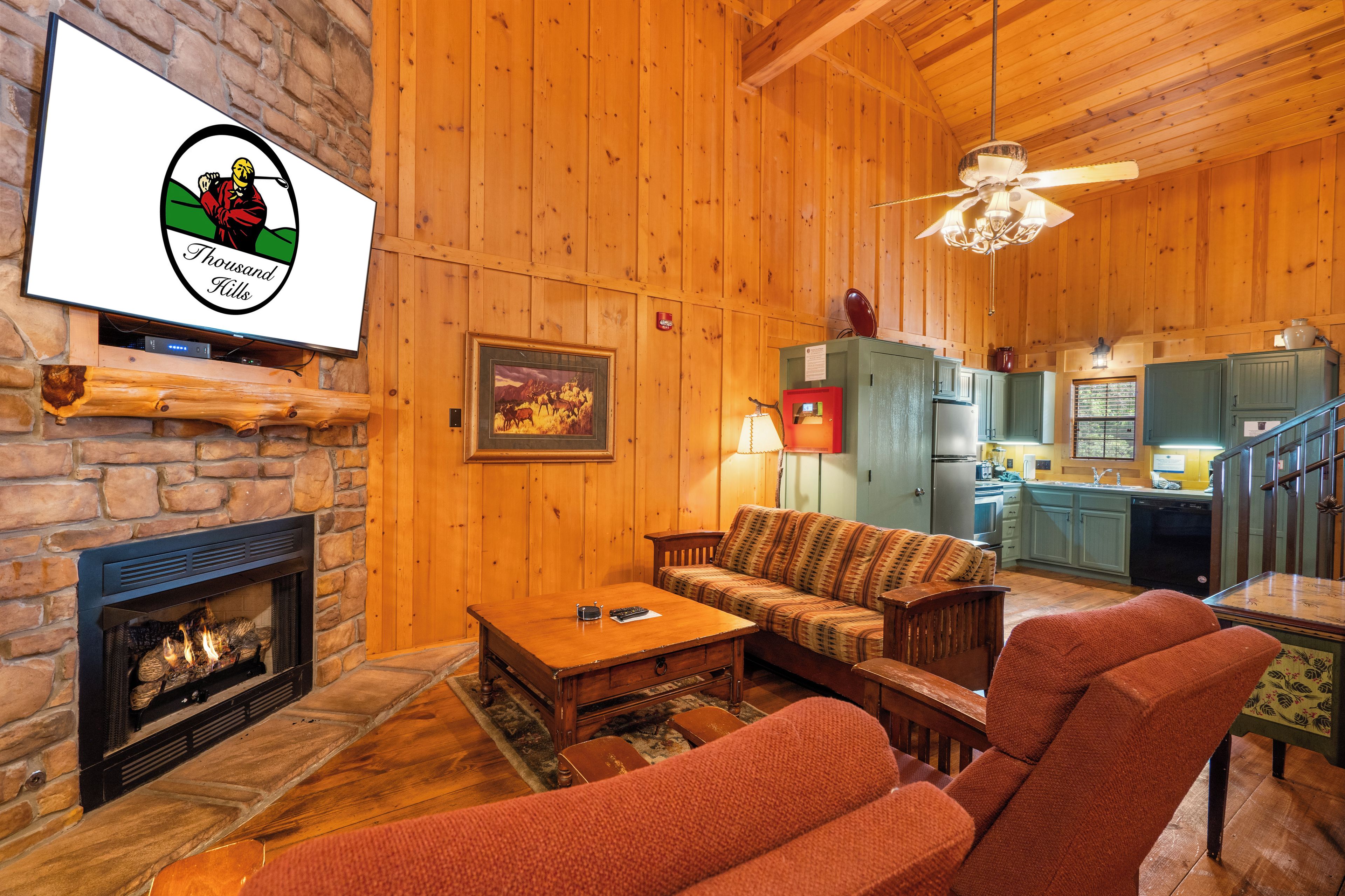 A cozy living room with a fireplace, a television mounted on a stone wall, a sofa, a coffee table, and a dining table with chairs.