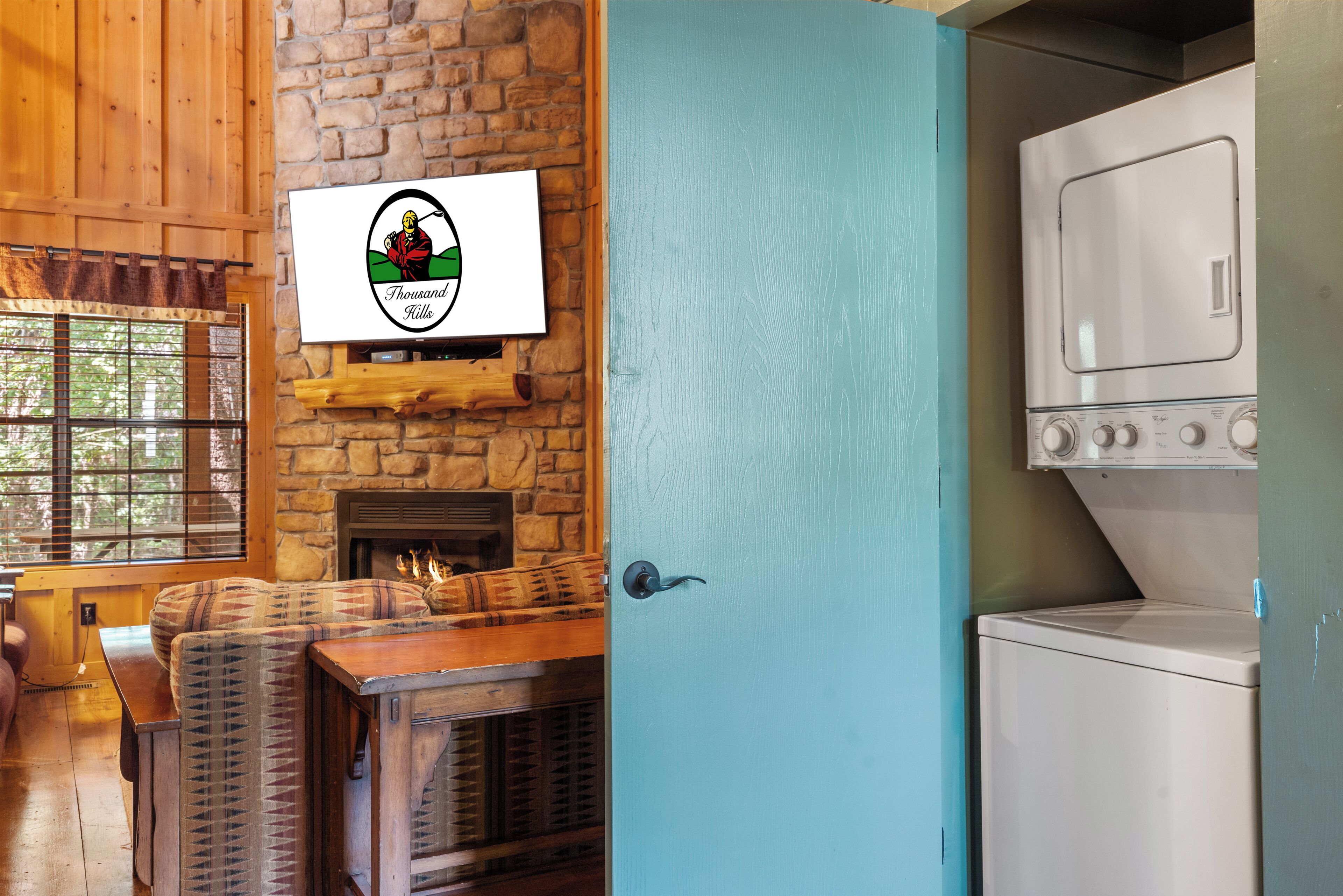 A room with a stone fireplace, a wooden dining table, and a blue door leading to a kitchen with a white appliance.