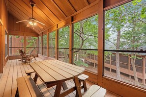 A wooden deck with a table and chairs, large windows, and a ceiling fan. - Cabins at Green Mountain (Branson)