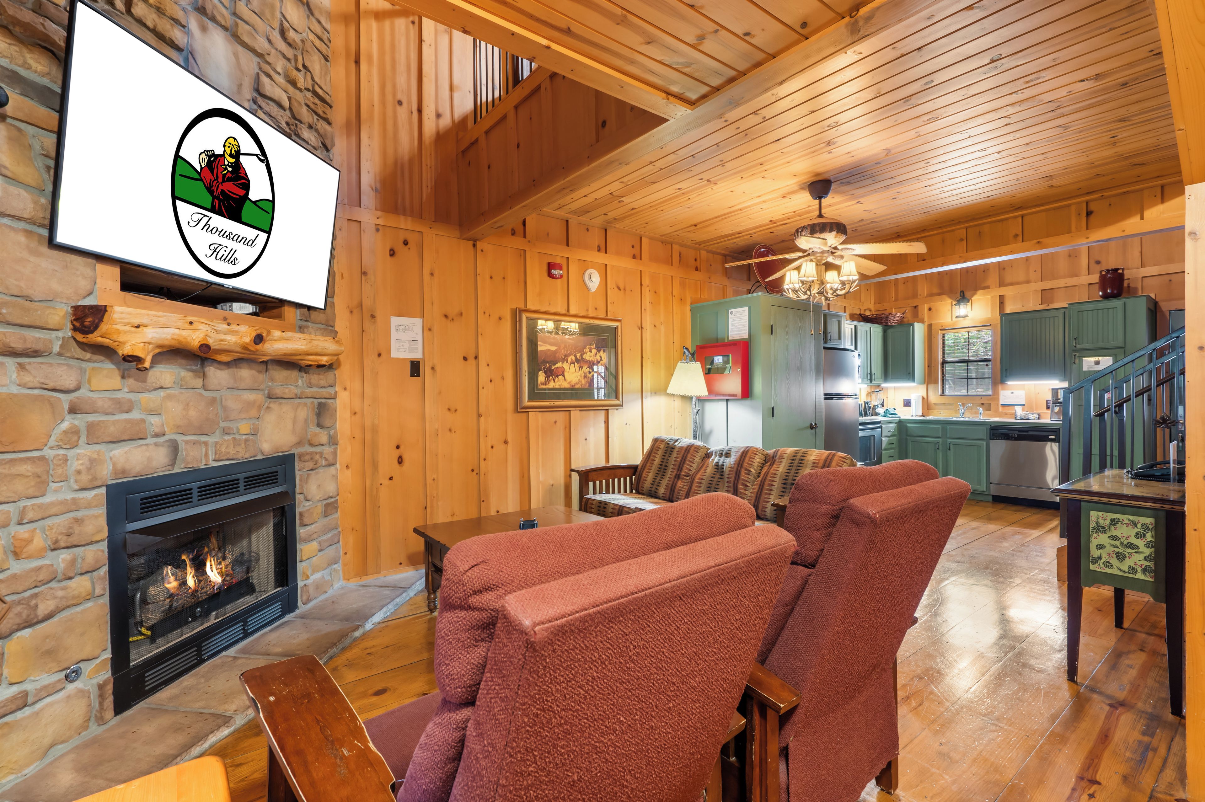 A cozy cabin interior with a stone fireplace, wooden furniture, and a kitchen area.