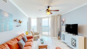 A spacious living room with a sofa, coffee table, and television. - Palacio Condominiums (Pensacola)
