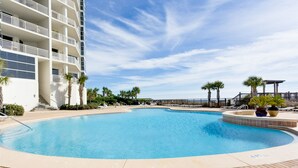 A swimming pool surrounded by a brick patio, palm trees, and a multi-story building with balconies. - Palacio Condominiums (Pensacola)