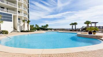 Relax by the clear blue pool surrounded by palm trees and a multi-story building with balconies.