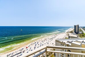 A beach view from a balcony with a clear sky, a sandy beach, and a tall building in the background. - Palacio Condominiums (Pensacola)