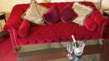 A red velvet sofa with decorative pillows and a glass table with a bottle and two glasses.