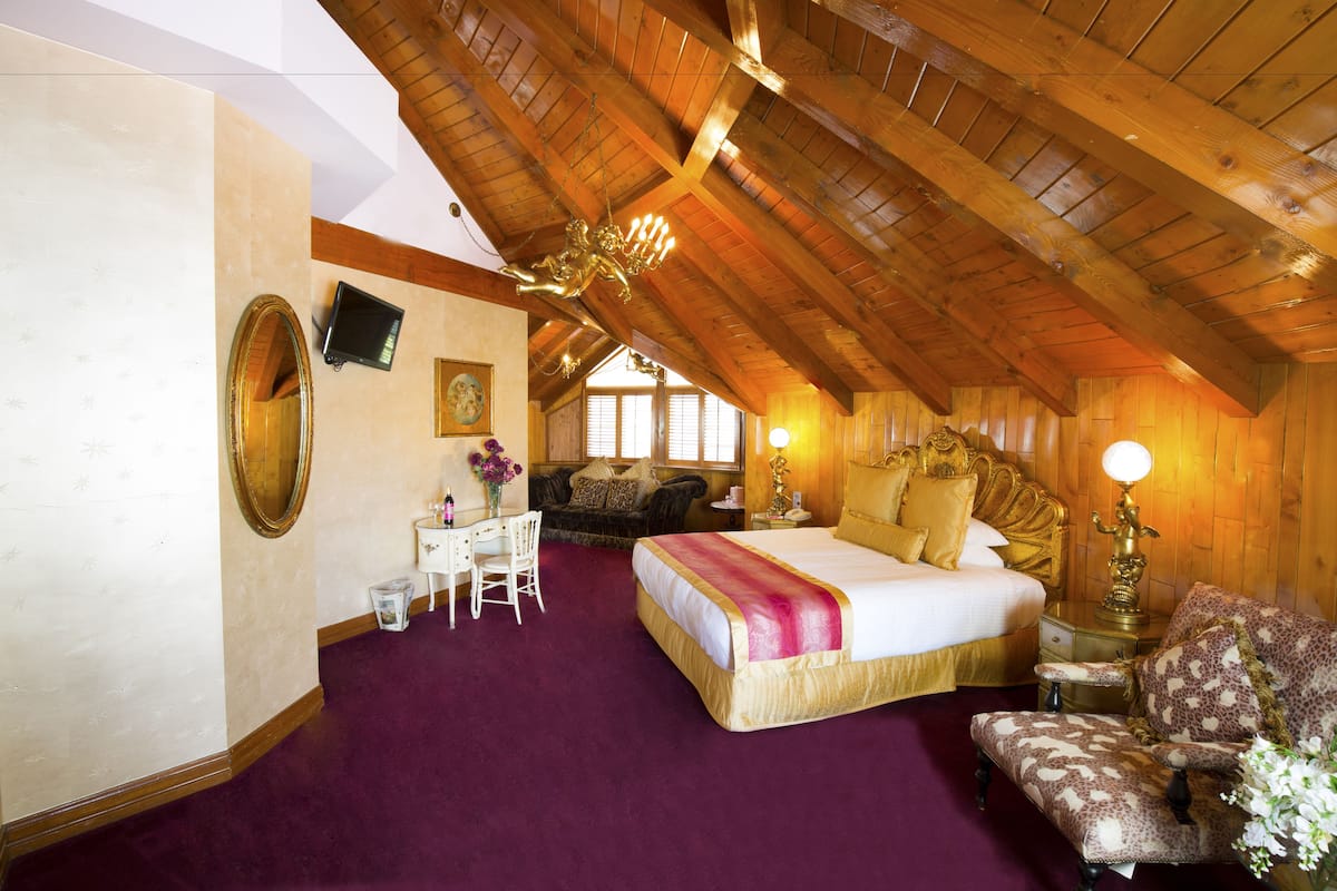 Ein geräumiges Schlafzimmer mit einem großen Bett, einem Schreibtisch und einem Sessel, mit Holzbalken an der Decke und einem violetten Teppich.