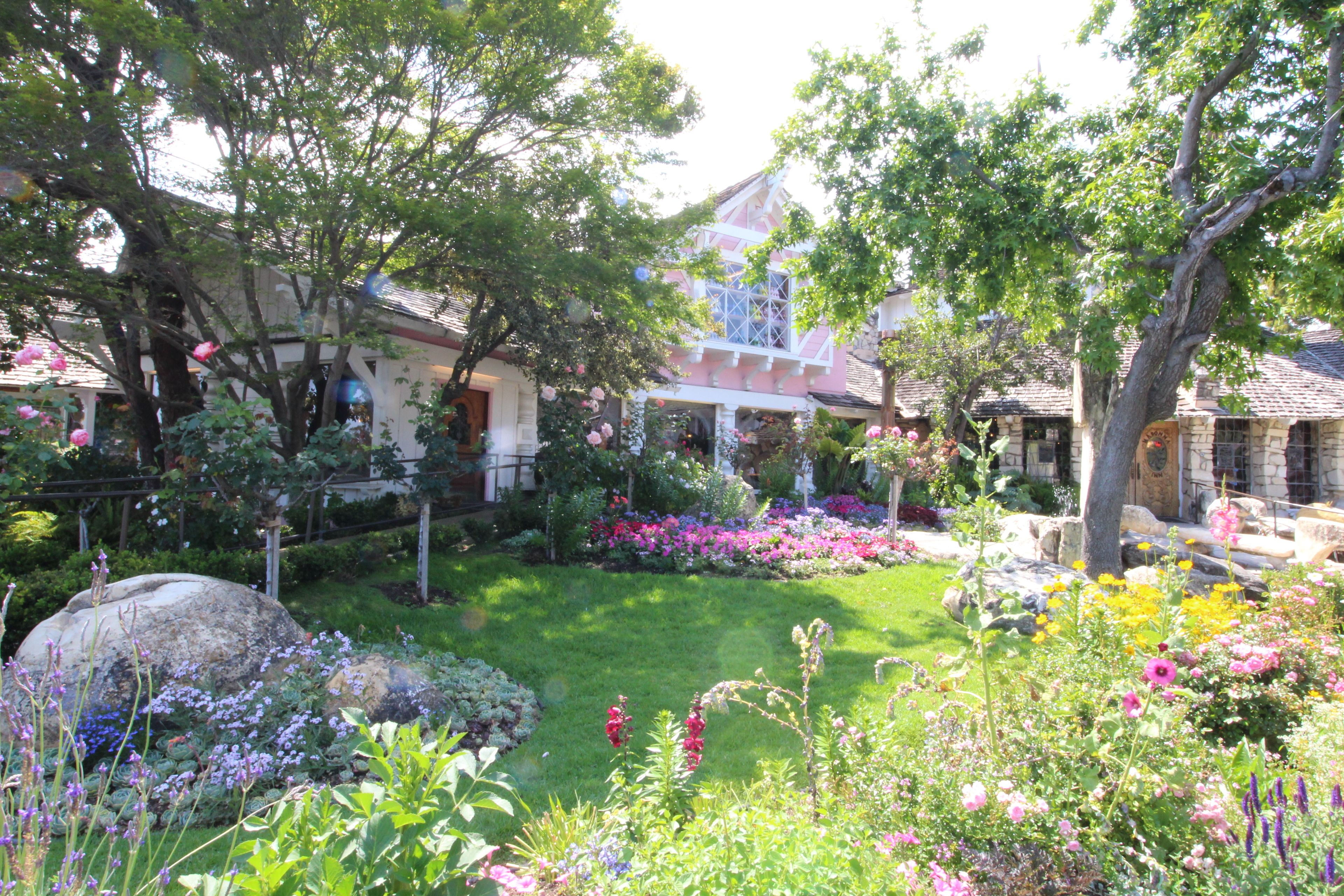 Un jardin où s’épanouit une grande variété de fleurs, avec une maison en arrière-plan.