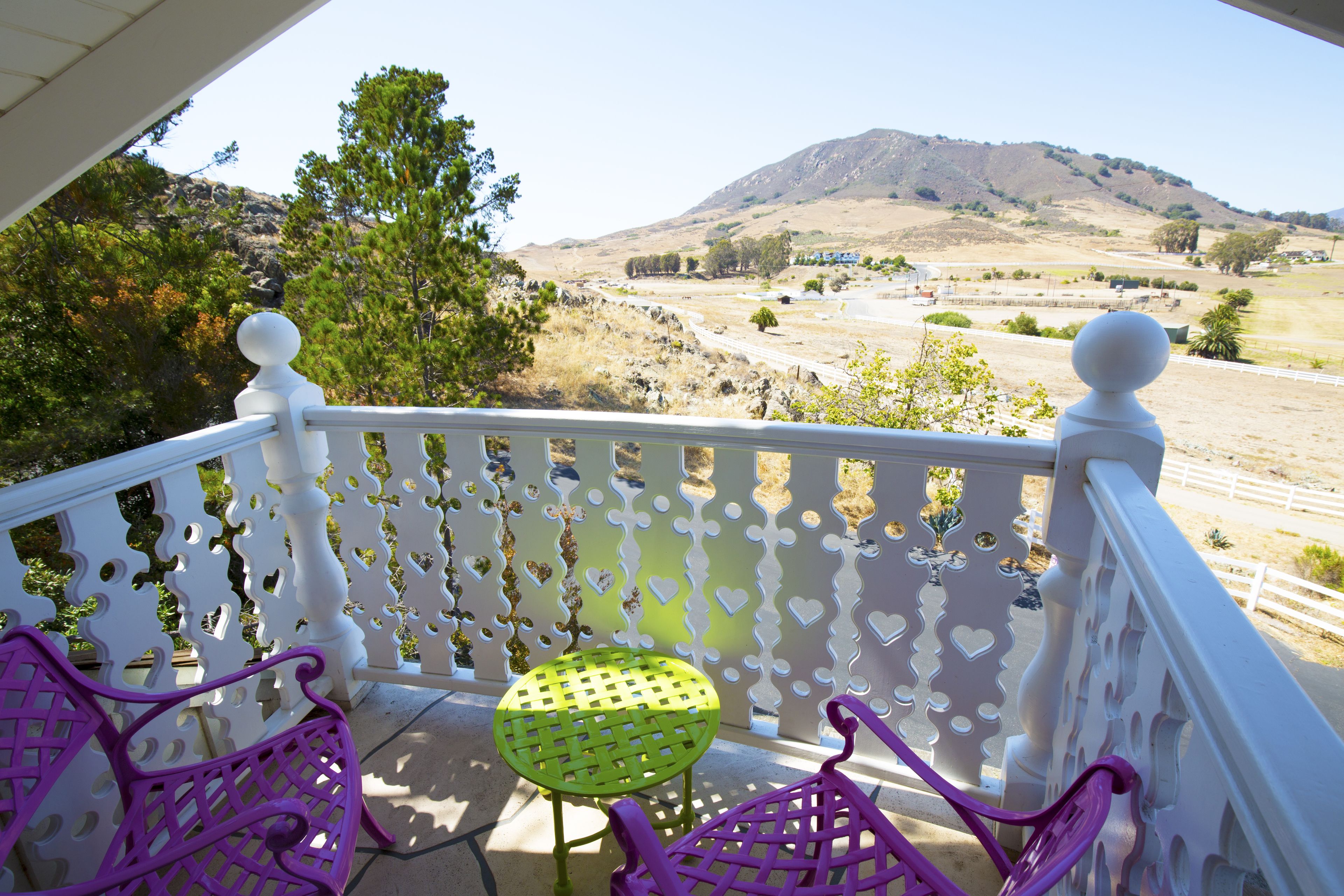 A balcony with white railings, a green table, and purple chairs.