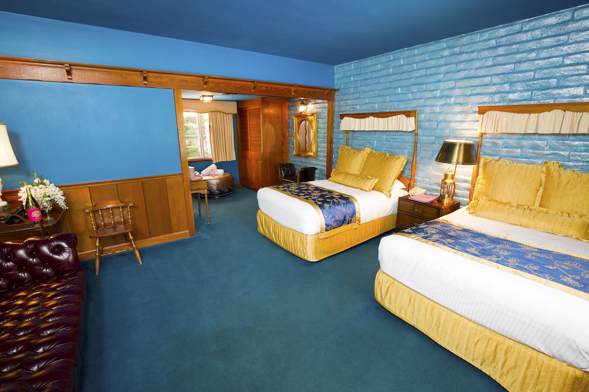 Ein Hotelzimmer mit zwei Betten, einem Holzstuhl, einem Schreibtisch mit Lampe und einer blauen Ziegelwand.