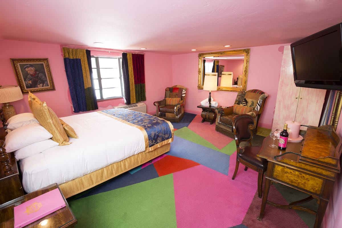 Ein Hotelzimmer mit einem großen Bett, einem Schreibtisch, einem Sessel, einem Fernseher und einem Spiegel.